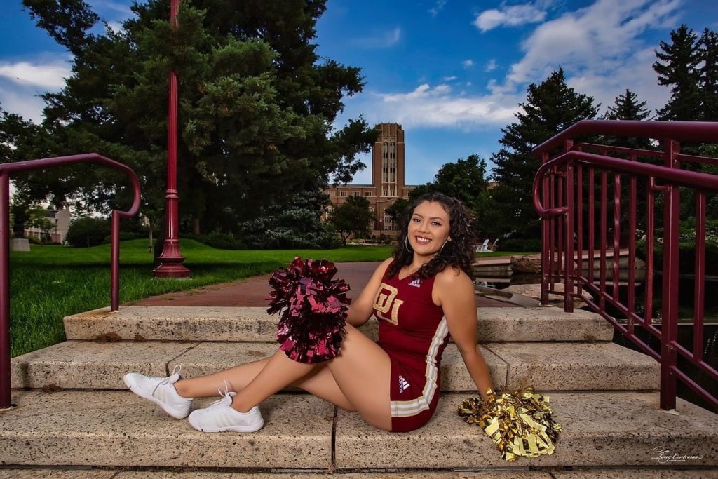 DSF Scholar Gigi Granados sits on the steps at her DU campus posing in her cheerleading uniform and smiling.